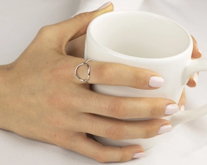 Close-up of minimalist silver geometric ring worn on hand against a white ceramic backdrop