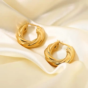 Close-up of golden twisted hoop earrings on white satin fabric with soft lighting