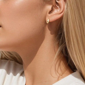 Close-up of polished gold teardrop stud earring worn by model in soft natural light