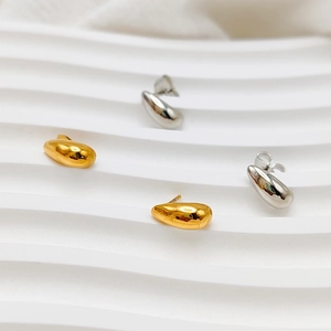 Polished gold and silver teardrop stud earrings displayed on a white textured tray