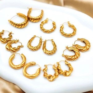 Close-up of gold twisted hoop earrings set with croissant and rope textures on white ceramic
