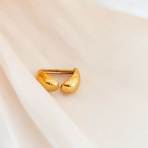 Close-up of golden teardrop earrings on elegant beige silk fabric with high-gloss finish