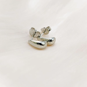 Close-up of silver teardrop stud earrings with polished finish on soft pink silk
