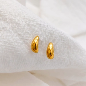Close-up of polished gold teardrop stud earrings on a textured white fabric background