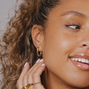 Close-up of polished gold hoop earring and geometric rings on a model for jewelry styling