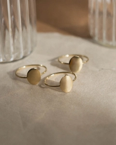 Detailed view of three minimalist gold-plated oval signet rings on grey textured paper