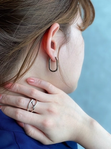 Close-up of minimalist silver oval hoop earring and cross-design ring on a female model