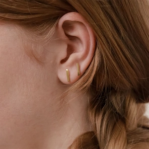 Close-up of elegant gold rectangular bar stud earrings worn by a model in a minimal style