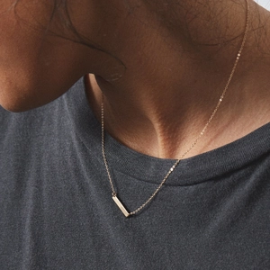 Minimalist gold bar pendant necklace on a thin chain worn by a female model