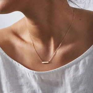Detail of a minimalist gold rectangular bar pendant necklace on a textured white top