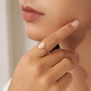 Close-up of minimalist rose gold oval ring worn on finger with polished metal finish