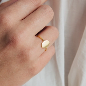 Minimalist oval flat surface gold-plated stainless steel ring shown on a finger