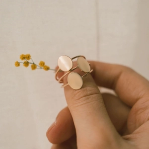 Detail of three minimalist rose gold oval rings worn by a model in a warm elegant setting