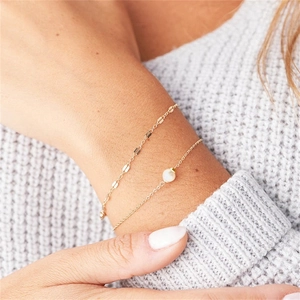 Detail of layered gold stainless steel chains with a single white pearl on a knited sleeve