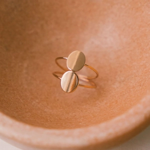 Macro view of minimalist gold-plated ring with double oval motif in a clay bowl