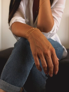 Detail of a minimalist double-layer gold chain bracelet on model with a small round pendant