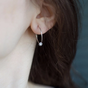 Close-up of minimalist silver stainless steel hoop earring with a small zircon stone