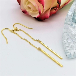 Detailed view of long gold-plated drop earrings with chain and bar on a floral background