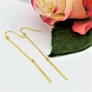 Detail of gold minimalist chain earrings with sleek bar pendant on white background