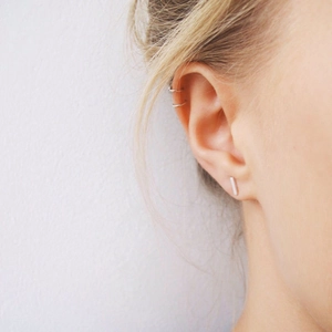 Close-up of minimalist stainless steel rectangular studs and hoop ear cuffs on model