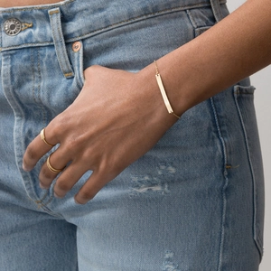 Close-up of minimalist gold bar bracelet with fine chain worn with denim jeans