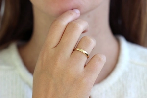 Minimalist gold-plated stainless steel band ring on a model's ring finger