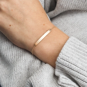 Close-up of a minimalist gold bar bracelet worn on wrist over a knitted sweater texture