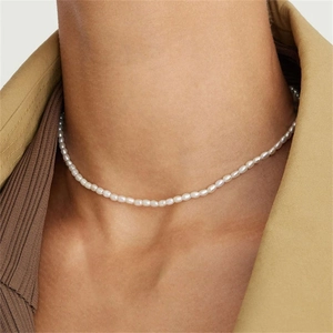 Gros plan d'un collier de perles ovales blanches porté avec un costume beige chic