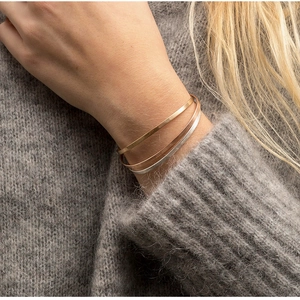 Minimalist polished steel bangles in gold, silver, and rose gold worn over a cozy sweater