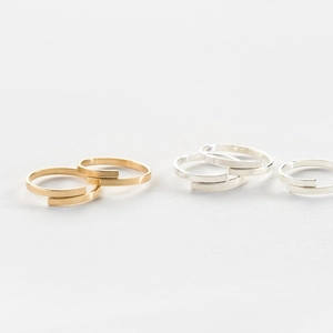 Anelli a fascia aperta minimalisti con finiture lucide in oro e argento su sfondo grigio