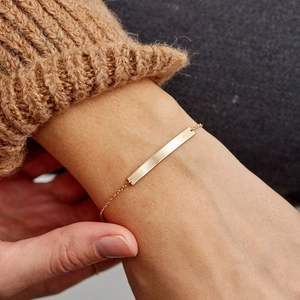Minimalist gold-plated polished bar bracelet for women worn on a brown knit sweater