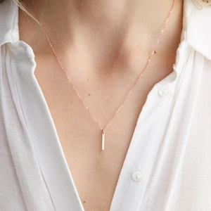Macro detail of rose gold bar necklace on model wearing a white shirt
