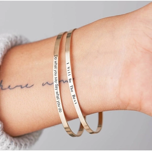 Close-up of polished gold bangles with inspirational engraved quotes on the wrist