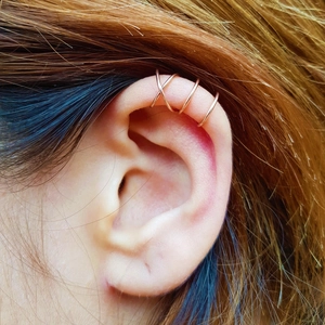 Macro shot of rose gold cross-wrapped ear cuff jewelry set on ear cartilage