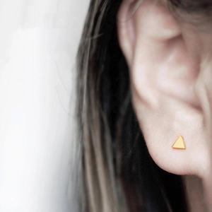 Macro shot of minimalist gold triangle stud earring worn on model's earlobe