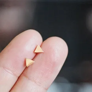 Close-up of minimalist gold-plated triangle stud earrings held between fingers