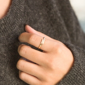 Dettaglio dell'anello incrociato minimalista in oro indossato su sfondo maglione grigio