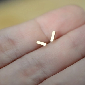 Detailed view of minimalist gold rectangular stud earrings showing compact size on skin