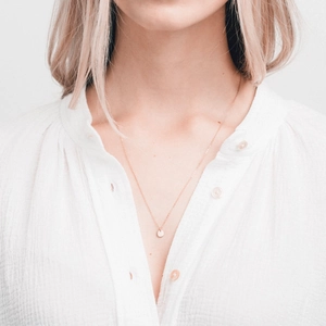 Gros plan d'un collier à pendentif rond doré porté avec une chemise blanche texturée