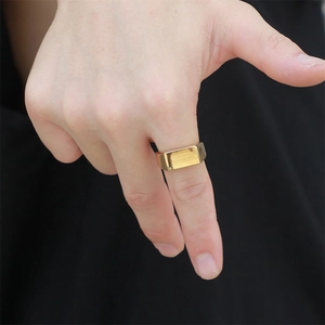 Close-up of a minimalist gold rectangular signet ring worn on a hand against black background