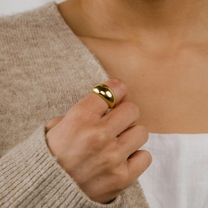 Gros plan sur une bague bombée dorée polie portée avec un pull en maille élégant