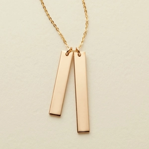 Detail view of double gold rectangular pendants on a sleek stainless steel chain