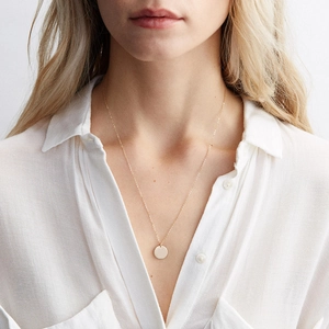 Gros plan détaillé d'un collier à pendentif rond doré minimaliste porté par un mannequin