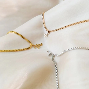 Dettaglio di ciondoli a cuore con lettere su catenine box in oro, argento e oro rosa