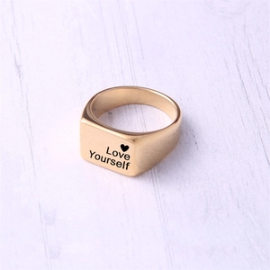 Close-up of golden square signet ring featuring Love Yourself engraving and heart icon