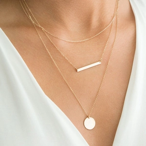Détail d'un collier doré à trois rangs avec pendentifs rectangle et rond sur modèle