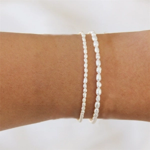 Detail showing layers of small white imitation pearls and baroque pearl bracelets on wrist