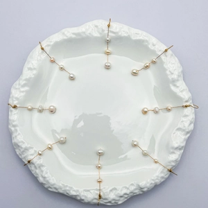Détail de huit longues boucles d'oreilles à pompons dorés et perles baroques sur plat blanc