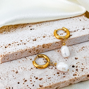 Detail of 14K gold plated hoops with baroque pearls on a textured stone surface
