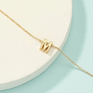 Vue macro du pendentif lettre M doré et de la chaîne délicate sur fond bleu